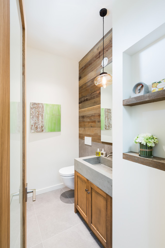 Cette photo montre un WC suspendu tendance en bois brun de taille moyenne avec un plan de toilette en béton, un carrelage gris, un placard à porte shaker, un mur blanc, un lavabo intégré et un sol blanc.