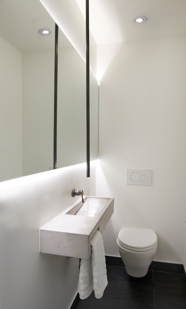 Immagine di un piccolo bagno di servizio contemporaneo con WC sospeso, pareti bianche, pavimento in ardesia, lavabo integrato e top in cemento