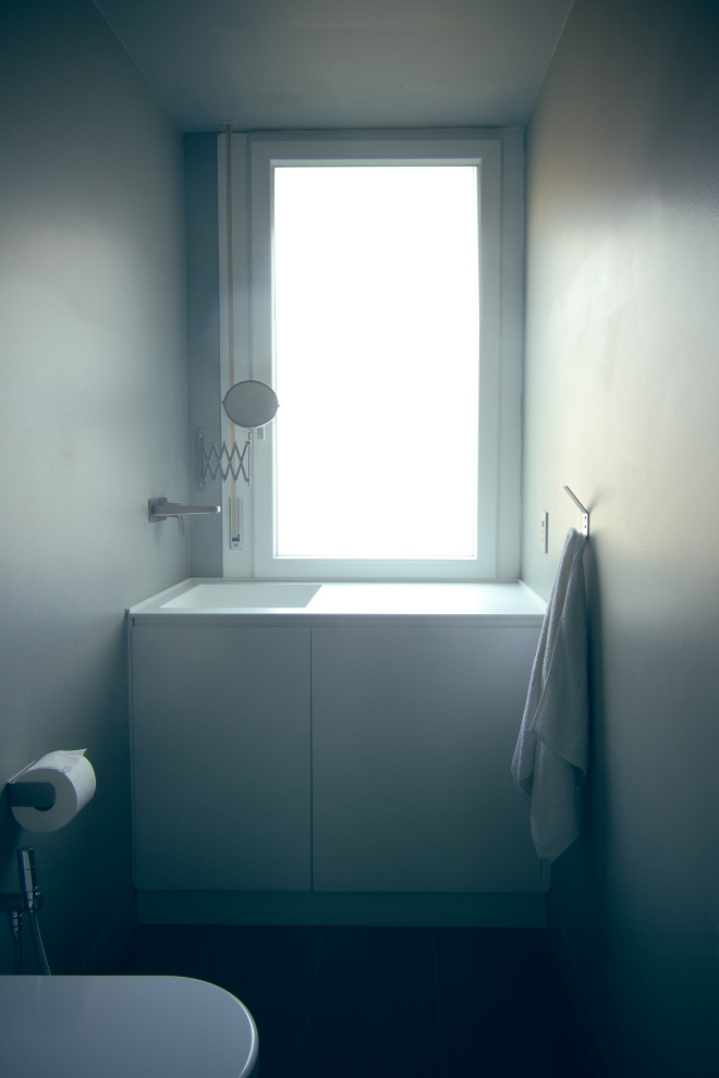 Réalisation d'un petit WC et toilettes design avec un placard à porte plane, des portes de placard blanches, un mur gris, un sol en calcaire et un plan de toilette en surface solide.