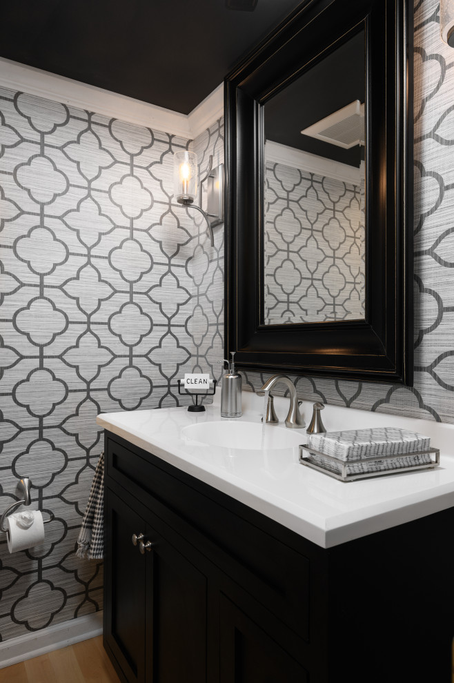 Inspiration for a small timeless light wood floor, beige floor and wallpaper powder room remodel in Philadelphia with flat-panel cabinets, black cabinets, a two-piece toilet, gray walls, an integrated sink, solid surface countertops, white countertops and a freestanding vanity
