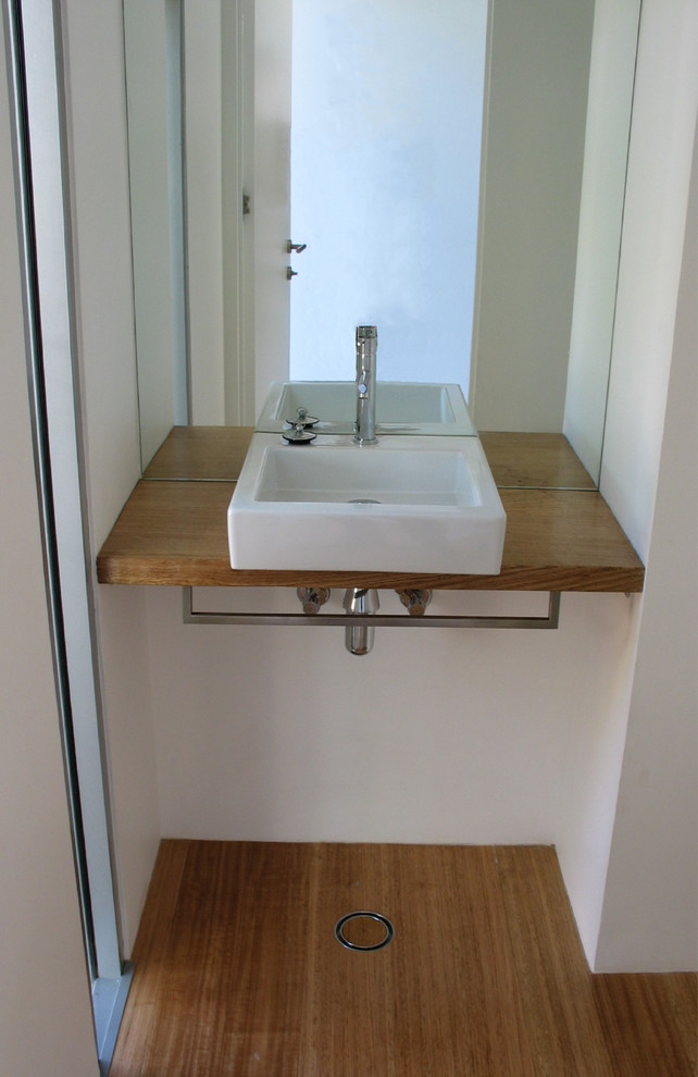 Bild på ett litet funkis toalett, med vita väggar, ljust trägolv, ett fristående handfat och träbänkskiva