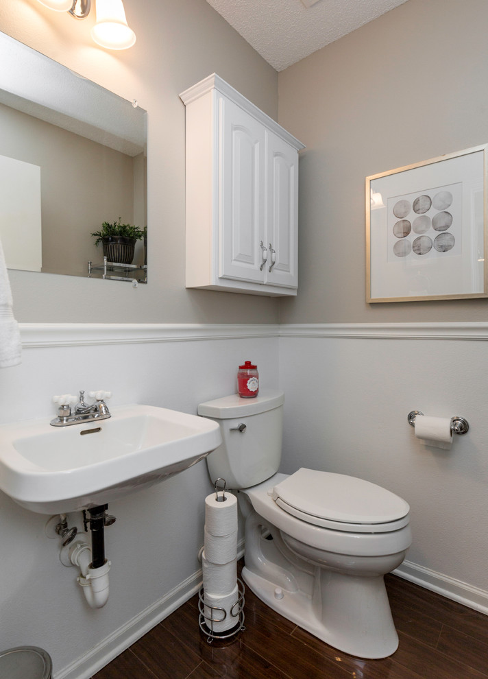 Exemple d'un petit WC et toilettes chic avec un placard avec porte à panneau surélevé, des portes de placard blanches, WC à poser, un mur gris, un sol en bois brun et un lavabo de ferme.