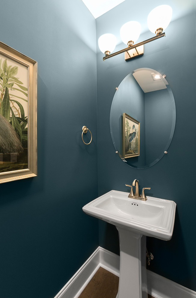 Klassisk inredning av ett toalett, med blå väggar, mellanmörkt trägolv, ett piedestal handfat och grått golv