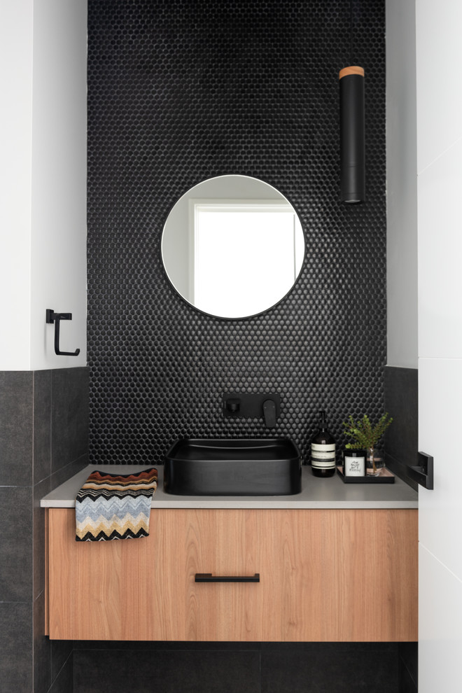 Réalisation d'un WC et toilettes urbain en bois brun avec un carrelage noir, mosaïque, carreaux de ciment au sol, une vasque, un plan de toilette en quartz modifié, un sol noir et un plan de toilette gris.