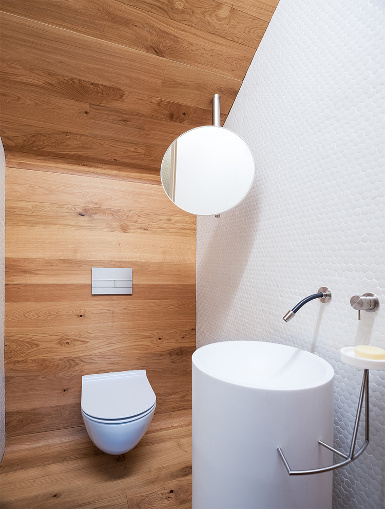 Idéer för att renovera ett litet funkis toalett, med en vägghängd toalettstol, vita väggar, mellanmörkt trägolv och ett piedestal handfat