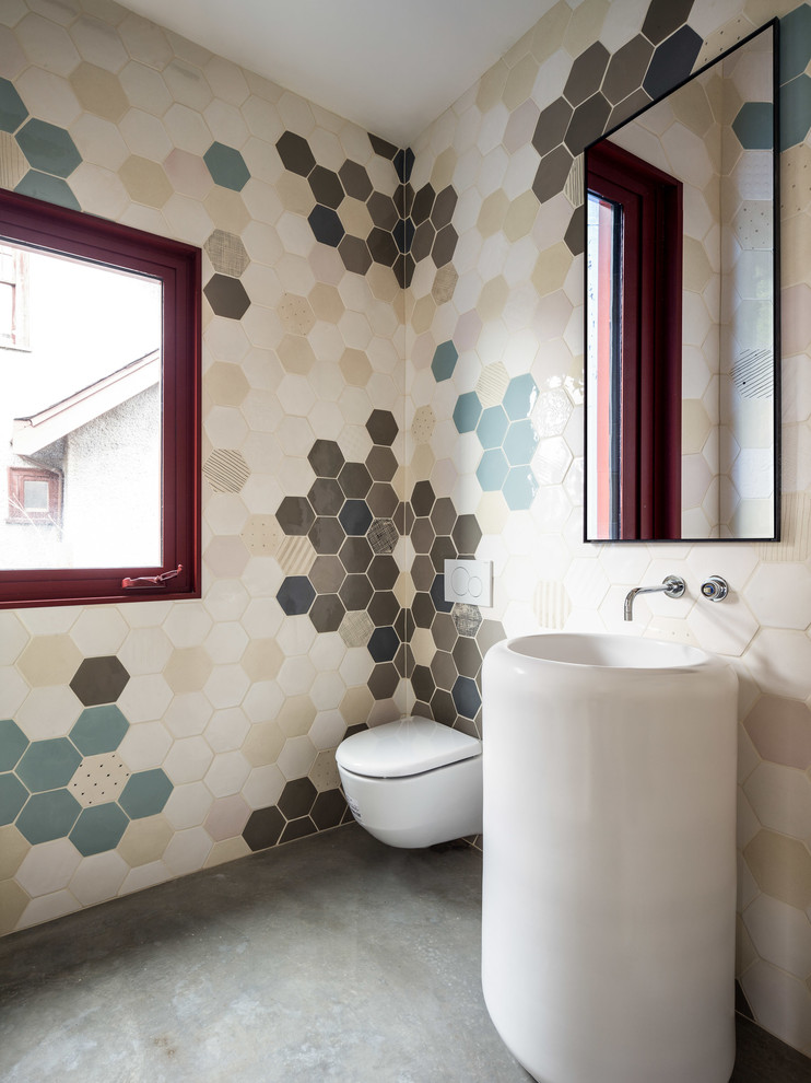 Ejemplo de aseo actual con sanitario de pared, paredes multicolor, suelo de cemento, lavabo con pedestal y suelo gris