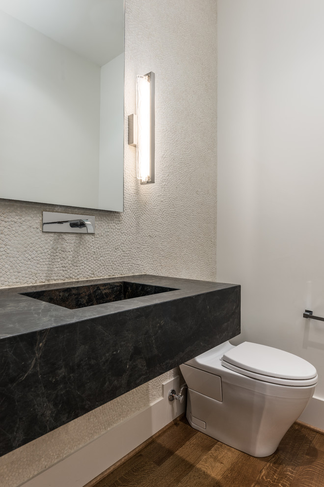 Medium sized modern cloakroom in Dallas with a one-piece toilet, beige tiles, pebble tiles, white walls, medium hardwood flooring, an integrated sink, marble worktops, brown floors and black worktops.