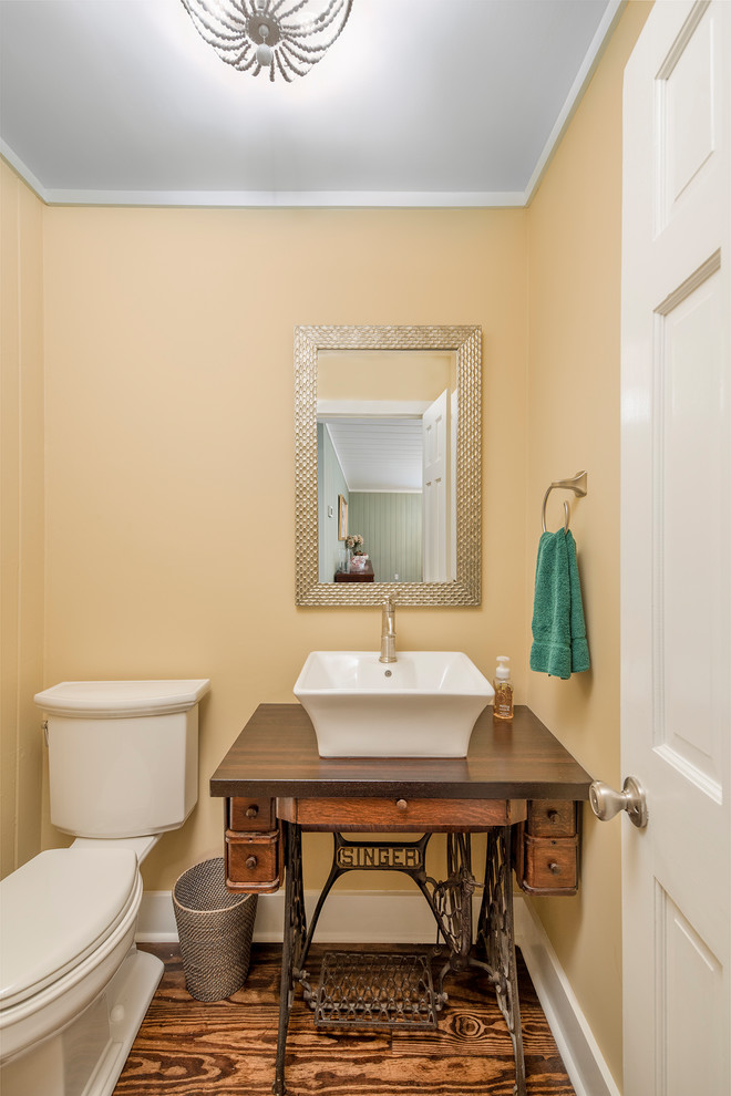 Пример оригинального дизайна: туалет в классическом стиле с фасадами островного типа, раздельным унитазом, желтыми стенами, паркетным полом среднего тона, настольной раковиной, столешницей из дерева и коричневой столешницей