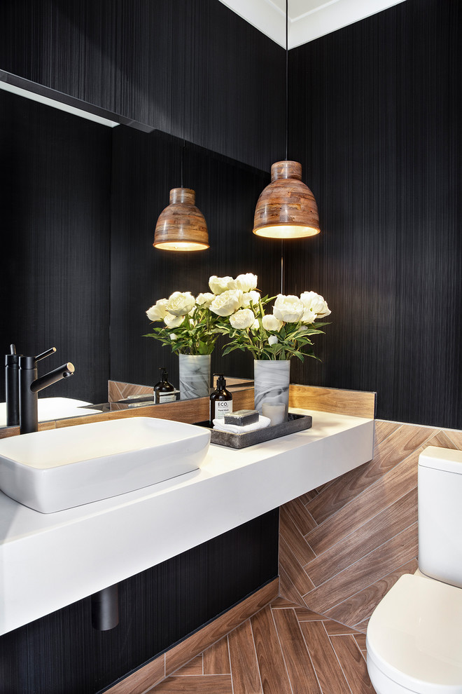 Réalisation d'un WC et toilettes design avec WC à poser, un carrelage marron, un mur noir, une vasque, un sol marron et un plan de toilette blanc.