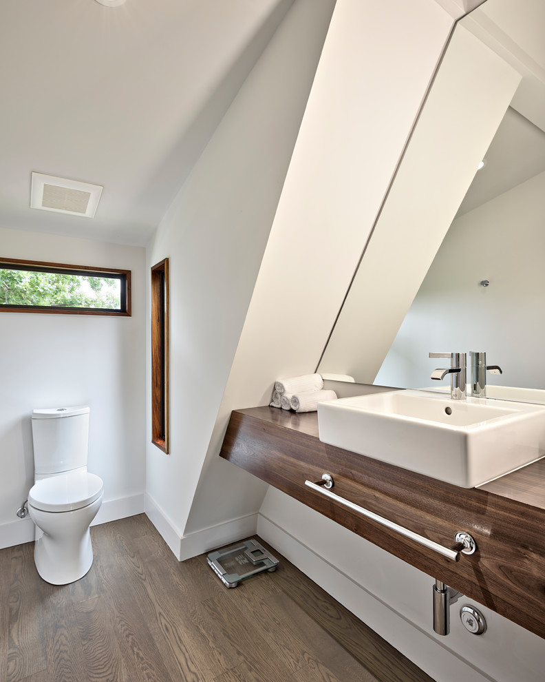 This is an example of a traditional cloakroom in Austin with medium wood cabinets, a wall mounted toilet, white walls, medium hardwood flooring, a built-in sink, wooden worktops and brown worktops.