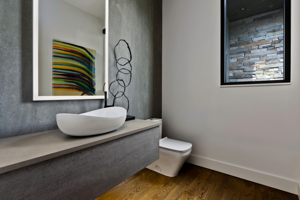 Imagen de aseo actual con paredes blancas, suelo de madera oscura, lavabo sobreencimera, suelo marrón y encimeras grises