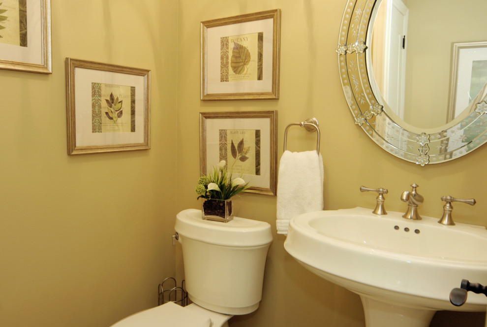 Inredning av ett klassiskt mellanstort toalett, med ett piedestal handfat, en toalettstol med separat cisternkåpa och gula väggar