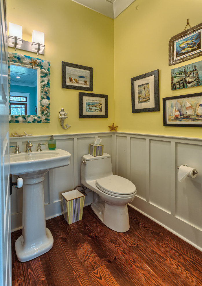 Aménagement d'un WC et toilettes bord de mer avec un mur jaune, parquet foncé, un lavabo de ferme et un sol marron.