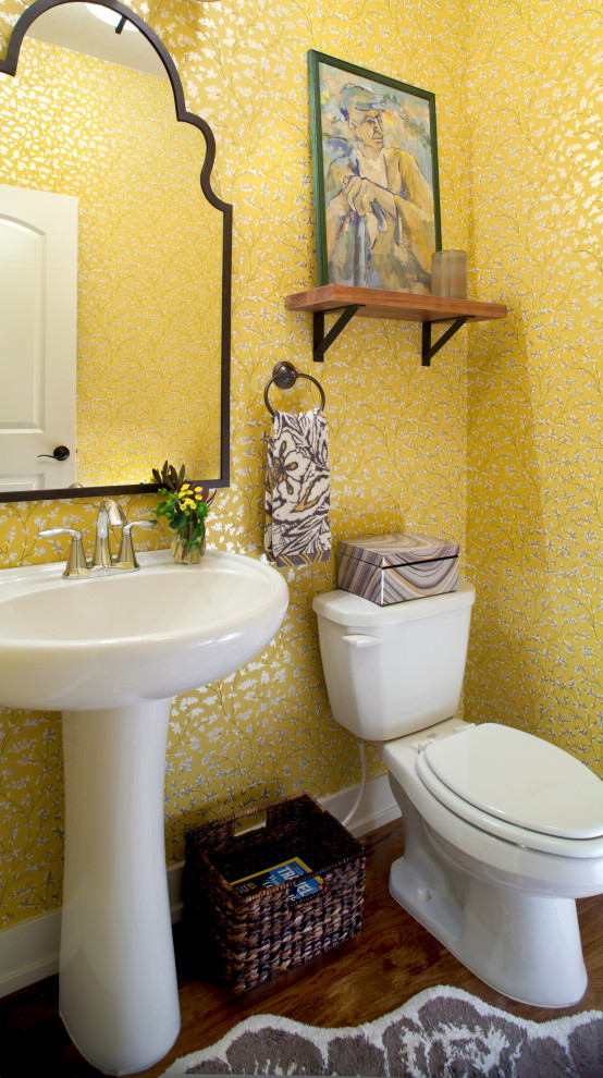Modelo de aseo tradicional renovado de tamaño medio con sanitario de dos piezas, paredes amarillas, lavabo con pedestal, suelo marrón y papel pintado