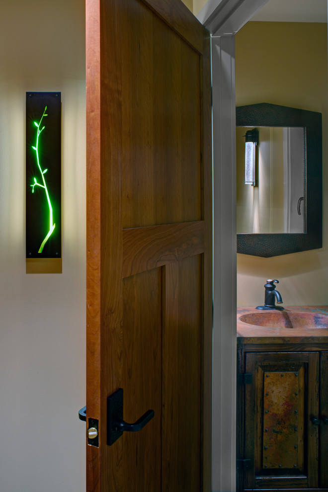 Foto på ett litet rustikt flerfärgad toalett, med luckor med upphöjd panel, skåp i slitet trä, en toalettstol med separat cisternkåpa, gula väggar, ett nedsänkt handfat och bänkskiva i akrylsten
