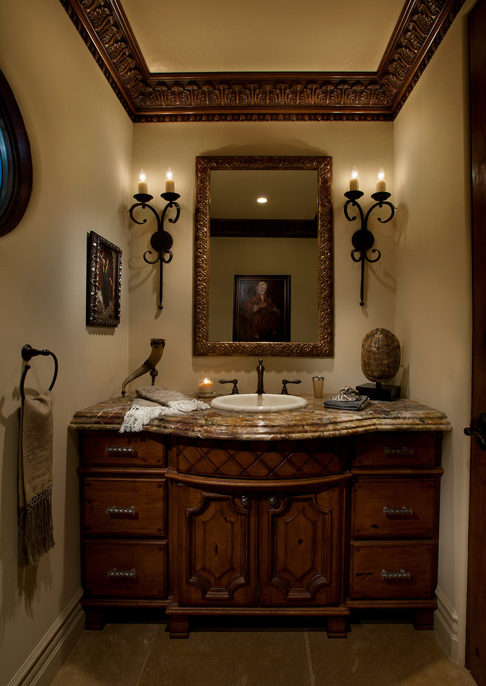 This is an example of a medium sized mediterranean cloakroom in Phoenix with freestanding cabinets, dark wood cabinets, beige tiles, stone tiles, beige walls, limestone flooring, a built-in sink and granite worktops.