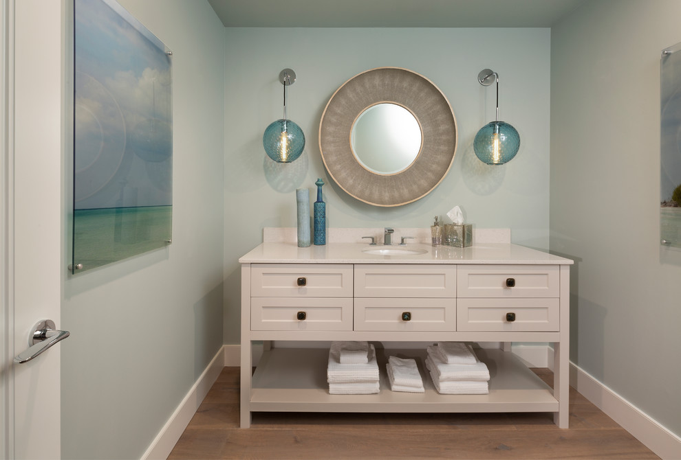 Foto på ett litet vintage beige toalett, med möbel-liknande, beige skåp, blå väggar, marmorbänkskiva, brunt golv, mellanmörkt trägolv och ett undermonterad handfat