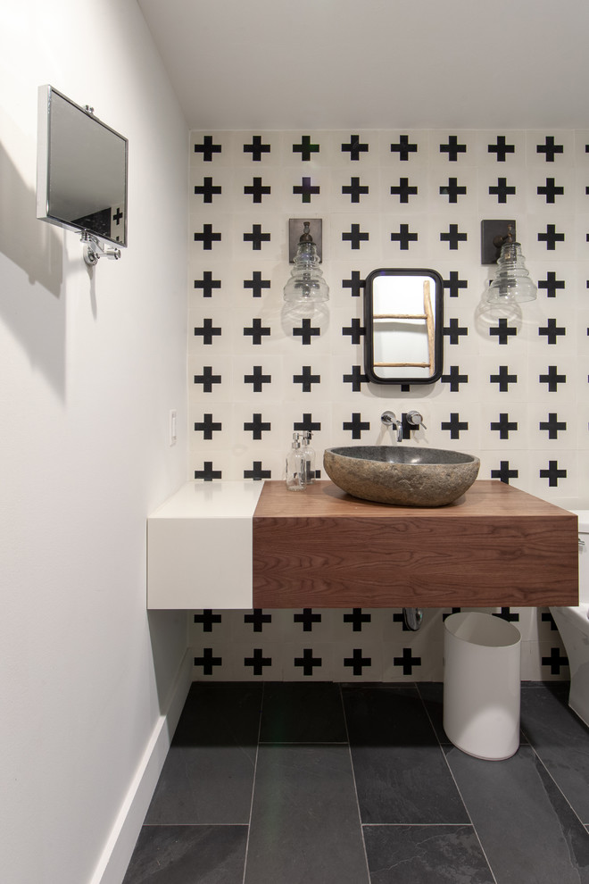 Inspiration for a farmhouse cloakroom in Charlotte with medium wood cabinets, black and white tiles, white walls, slate flooring, a vessel sink, wooden worktops, grey floors and brown worktops.