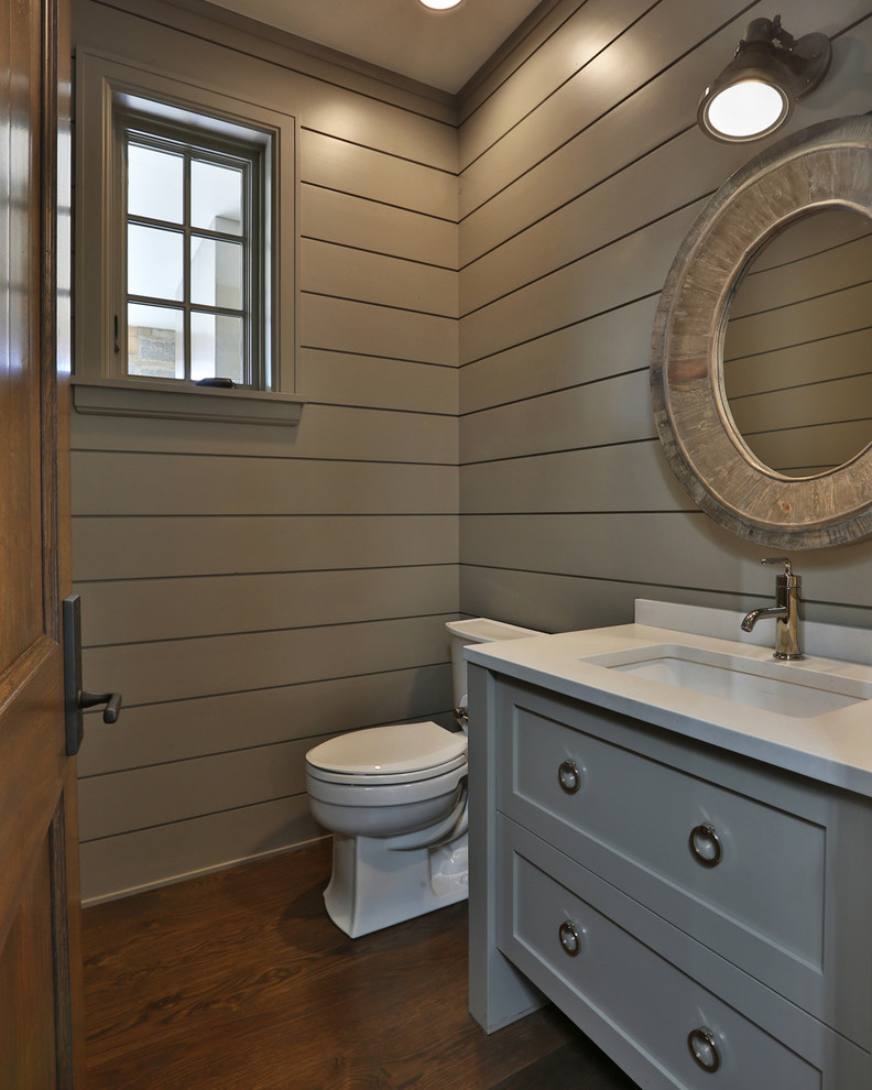 Aménagement d'un petit WC et toilettes campagne avec un placard à porte plane, des portes de placard grises, WC à poser, un carrelage beige, un mur beige, un sol en bois brun, un lavabo encastré, un sol marron et un plan de toilette blanc.