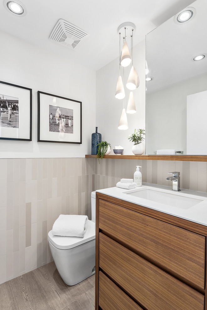Inspiration for a small contemporary cloakroom in Vancouver with flat-panel cabinets, medium wood cabinets, a two-piece toilet, grey tiles, porcelain tiles, white walls, light hardwood flooring, a submerged sink, engineered stone worktops, brown floors and white worktops.