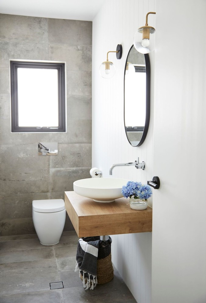 Inspiration för moderna toaletter, med möbel-liknande, skåp i ljust trä, en vägghängd toalettstol, grå kakel, cementkakel, cementgolv, laminatbänkskiva och grått golv