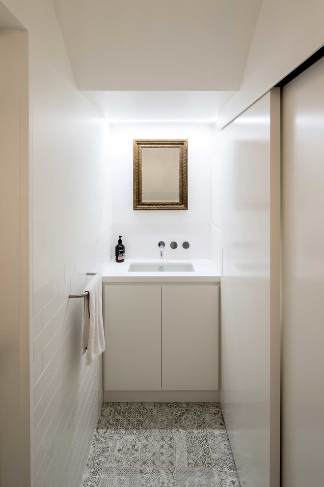 Moderne Gästetoilette mit flächenbündigen Schrankfronten, weißen Schränken, weißen Fliesen, Metrofliesen, weißer Wandfarbe, grauem Boden und weißer Waschtischplatte in Sydney