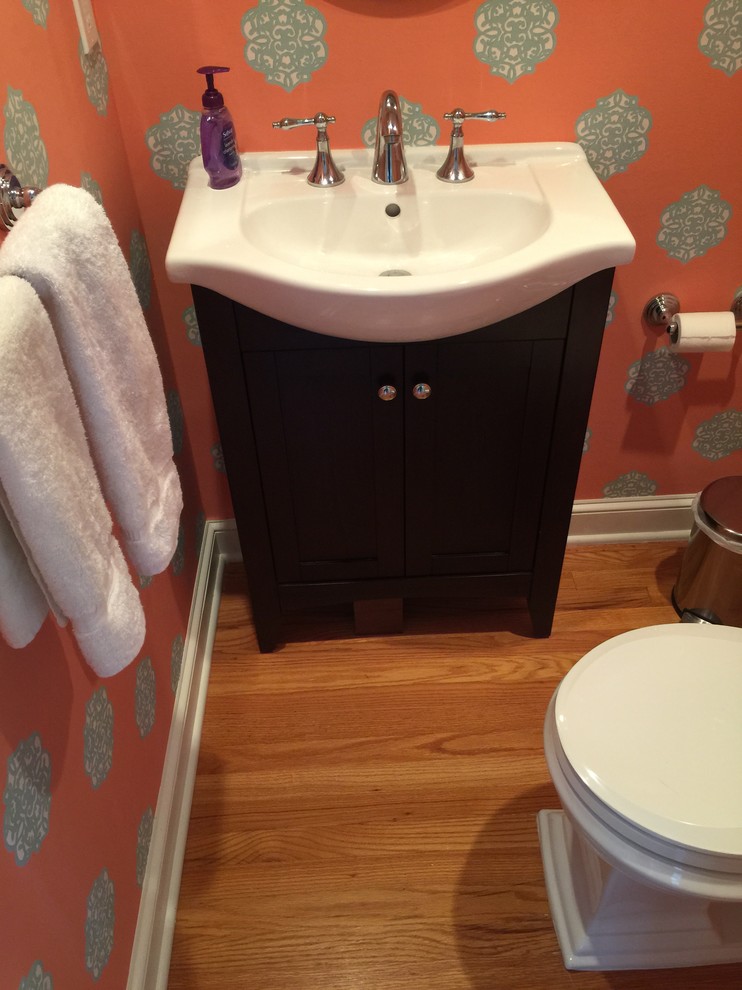 Inspiration for a mid-sized transitional light wood floor powder room remodel in New York with shaker cabinets, dark wood cabinets, a two-piece toilet, orange walls and a drop-in sink