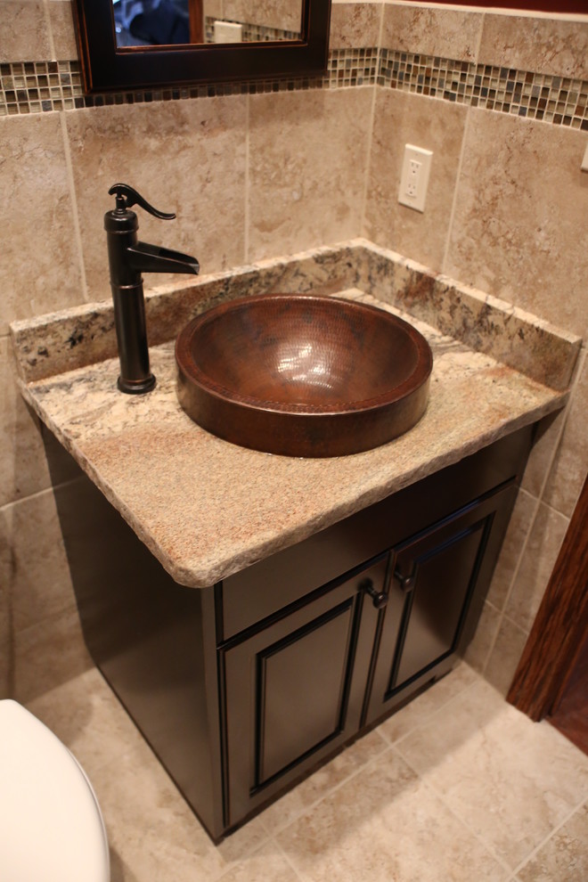 This is an example of a small rustic cloakroom in Chicago with raised-panel cabinets, dark wood cabinets, a one-piece toilet, mosaic tiles, travertine flooring, a vessel sink and granite worktops.