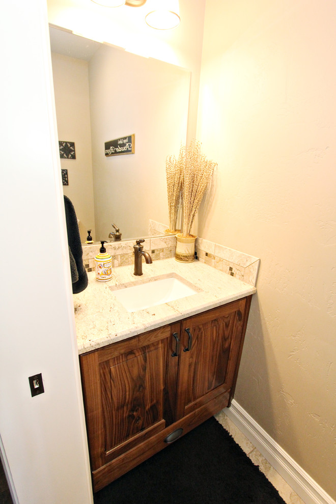 Cette photo montre un petit WC et toilettes chic en bois brun avec un placard avec porte à panneau surélevé, WC séparés, un carrelage beige, des plaques de verre, un mur beige, un sol en carrelage de céramique, un lavabo encastré, un plan de toilette en granite et un sol beige.