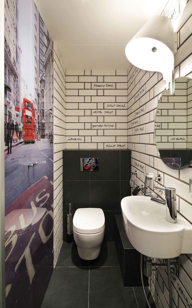 Modern inredning av ett toalett, med en vägghängd toalettstol, vita väggar, ett väggmonterat handfat, svart kakel och vit kakel