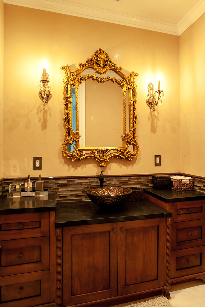 Пример оригинального дизайна: туалет среднего размера в средиземноморском стиле с фасадами в стиле шейкер, темными деревянными фасадами, унитазом-моноблоком, коричневой плиткой, стеклянной плиткой, бежевыми стенами, полом из известняка, настольной раковиной, столешницей из гранита, бежевым полом и черной столешницей