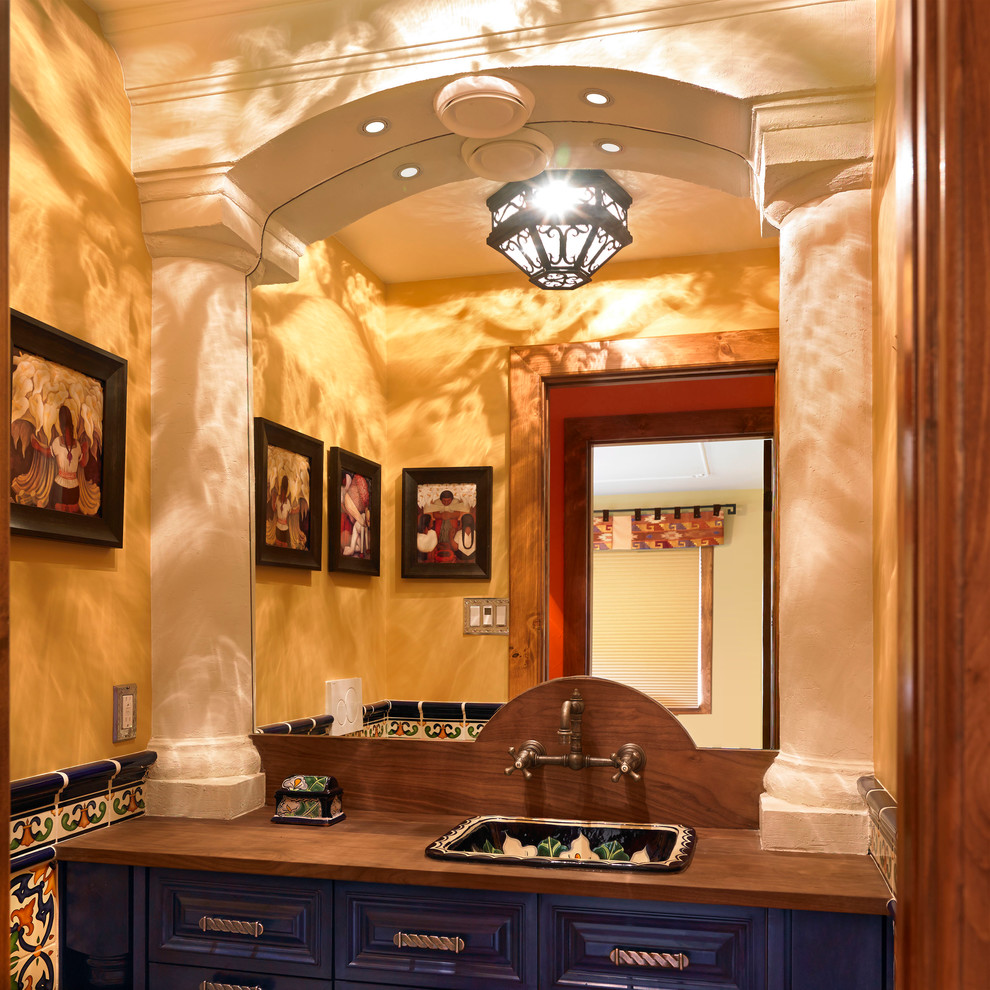 Idee per un bagno di servizio stile americano con lavabo da incasso, ante con bugna sagomata, ante blu, top in legno, piastrelle multicolore e top marrone