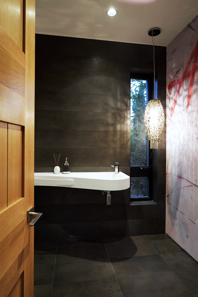 Aménagement d'un WC et toilettes contemporain de taille moyenne avec un lavabo intégré, un carrelage gris, un sol en carrelage de porcelaine, un plan de toilette en surface solide et un mur noir.