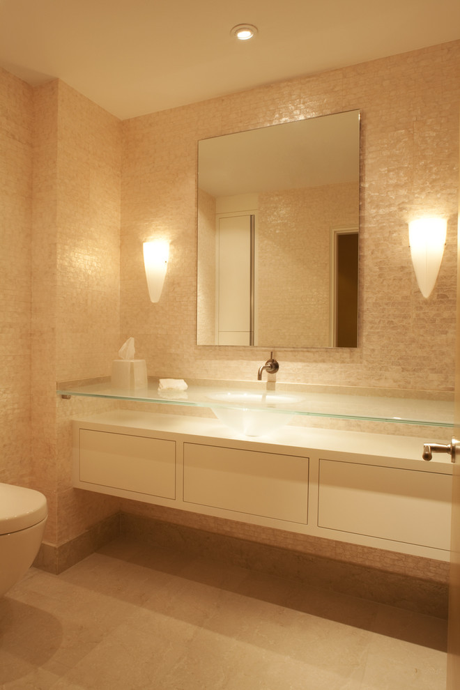Aménagement d'un WC et toilettes contemporain avec un plan de toilette en verre, un lavabo intégré et un carrelage beige.