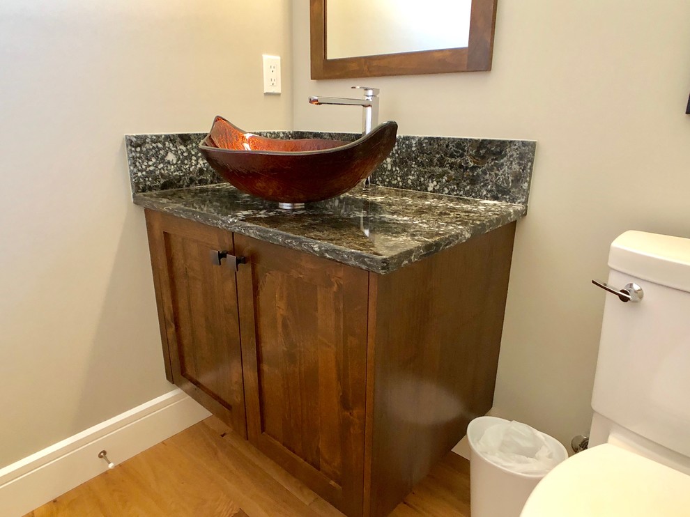 Cette image montre un petit WC et toilettes design avec un placard à porte shaker, des portes de placard marrons, un mur orange, parquet clair, une vasque, un plan de toilette en quartz modifié, un sol beige et un plan de toilette noir.