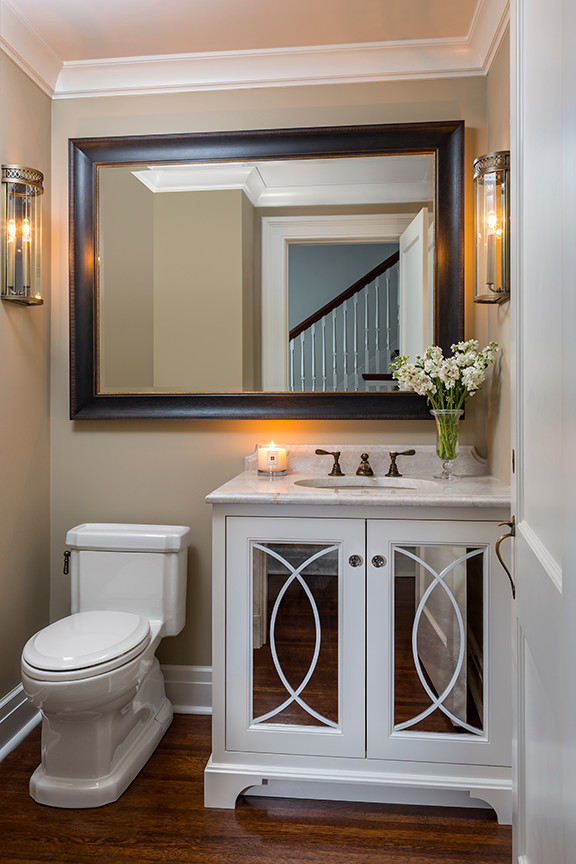 Bild på ett litet vintage vit vitt toalett, med vita skåp, en toalettstol med hel cisternkåpa, beige väggar, mellanmörkt trägolv, ett undermonterad handfat, bänkskiva i kvartsit och luckor med glaspanel