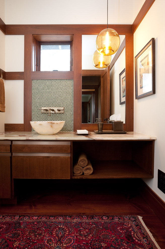 Klassisk inredning av ett litet toalett, med ett fristående handfat, släta luckor, bänkskiva i onyx, grön kakel, mosaik, vita väggar, mörkt trägolv och skåp i mörkt trä