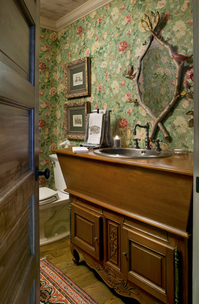 Klassisk inredning av ett brun brunt toalett, med ett nedsänkt handfat, luckor med upphöjd panel, träbänkskiva och skåp i mörkt trä