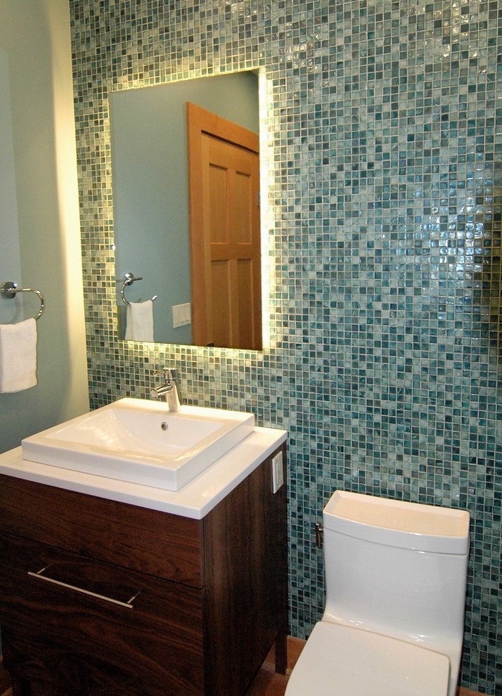 Kleine Klassische Gästetoilette mit verzierten Schränken, dunklen Holzschränken, Toilette mit Aufsatzspülkasten, blauen Fliesen, Glasfliesen, grüner Wandfarbe, braunem Holzboden, Quarzwerkstein-Waschtisch, Aufsatzwaschbecken und braunem Boden in Portland Maine
