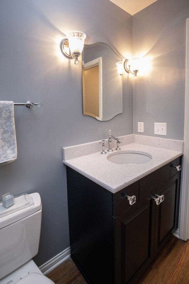 Design ideas for a small classic cloakroom in Indianapolis with raised-panel cabinets, blue cabinets, blue walls, medium hardwood flooring, a wall-mounted sink, engineered stone worktops, brown floors and white worktops.