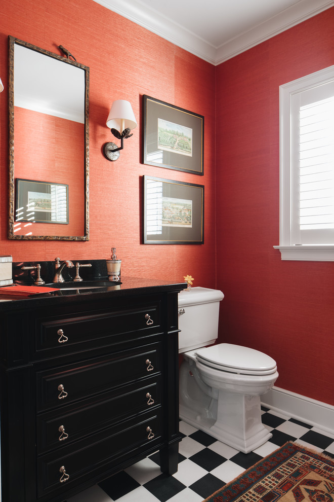 Foto på ett vintage svart toalett, med möbel-liknande, svarta skåp, en toalettstol med separat cisternkåpa, röda väggar, ett undermonterad handfat och flerfärgat golv