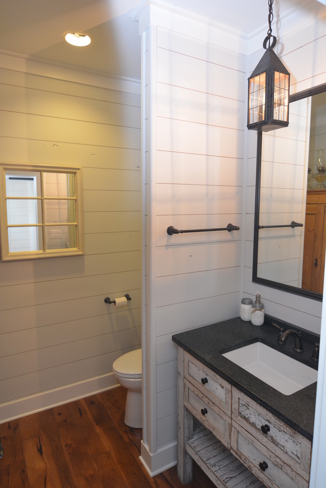 Bild på ett mycket stort lantligt toalett, med möbel-liknande, skåp i slitet trä, en toalettstol med hel cisternkåpa, vita väggar, mellanmörkt trägolv, ett undermonterad handfat och granitbänkskiva