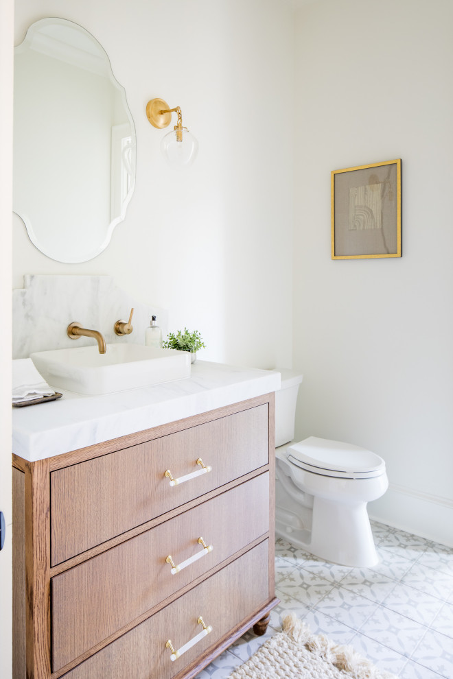 Inspiration for a mid-sized transitional cement tile floor and gray floor powder room remodel in Atlanta with furniture-like cabinets, light wood cabinets, white walls, a vessel sink, marble countertops and white countertops