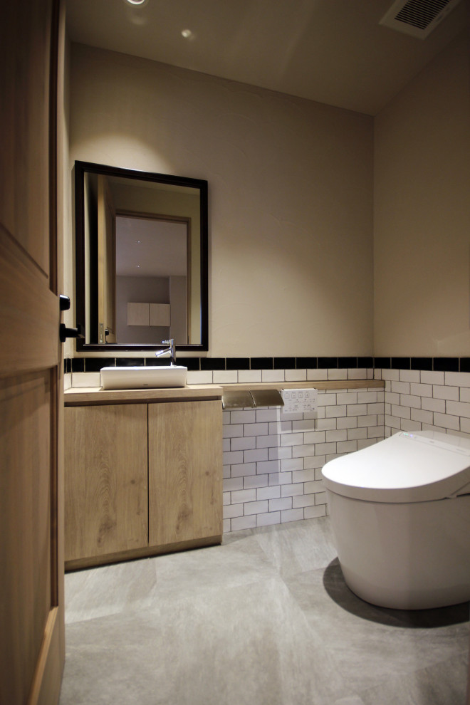 Exemple d'un petit WC et toilettes chic en bois brun avec un placard en trompe-l'oeil, WC à poser, un carrelage blanc, des carreaux de porcelaine, un mur blanc, sol en stratifié, une vasque, un plan de toilette en bois, un sol gris et un plan de toilette beige.