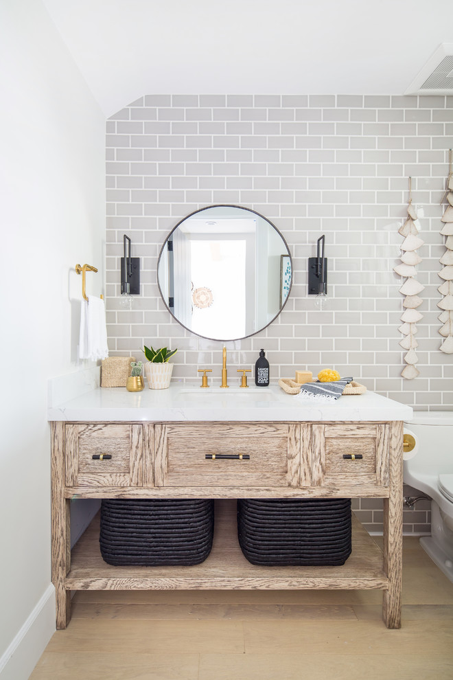 Inspiration for a nautical cloakroom in Orange County with freestanding cabinets, light wood cabinets, a one-piece toilet, grey tiles, metro tiles, light hardwood flooring, a submerged sink, beige floors and white worktops.