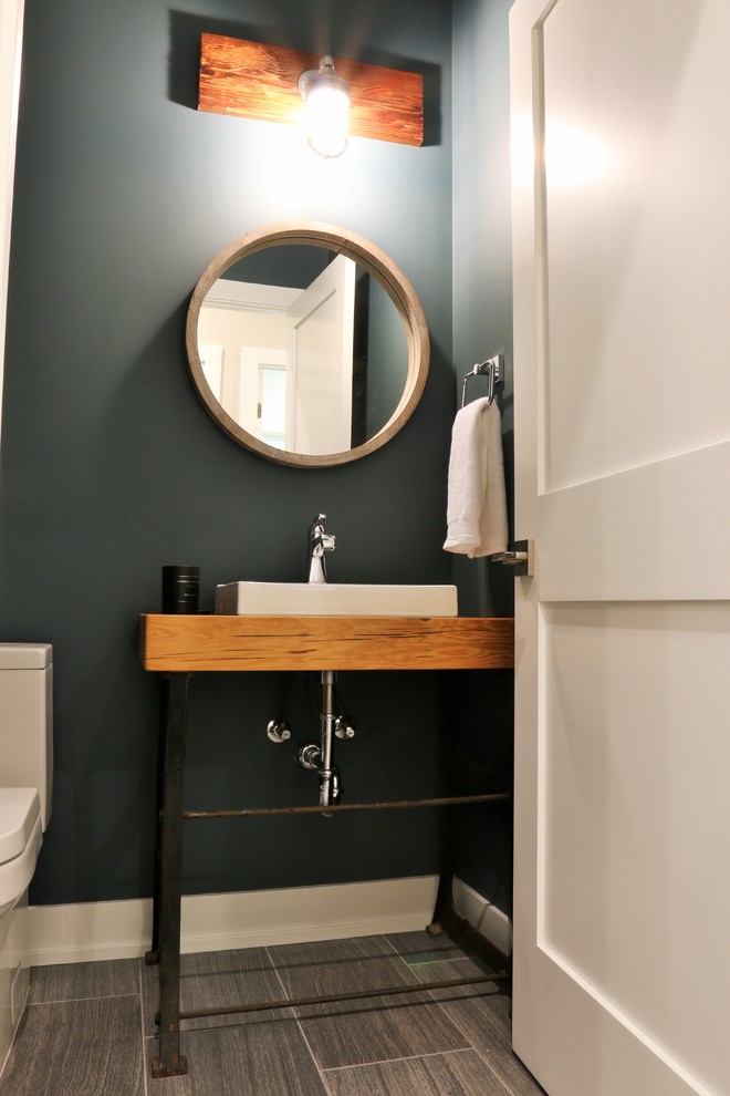 グランドラピッズにある中くらいなインダストリアルスタイルのおしゃれなトイレ・洗面所 (分離型トイレ、磁器タイル、磁器タイルの床、青い壁、ベッセル式洗面器、木製洗面台、ブラウンの洗面カウンター) の写真