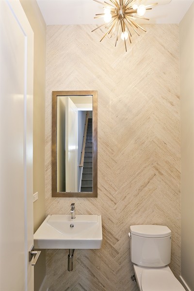 Esempio di un piccolo bagno di servizio moderno con nessun'anta, WC a due pezzi, piastrelle beige, piastrelle in pietra, pareti beige, parquet chiaro e lavabo sospeso