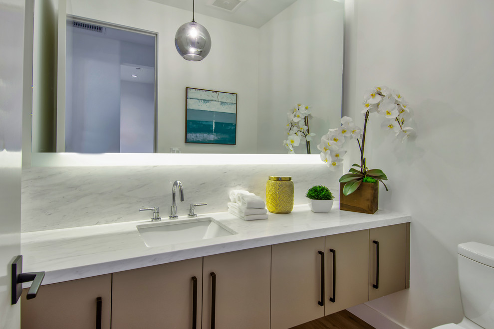 Moderne Gästetoilette mit flächenbündigen Schrankfronten, beigen Schränken, Wandtoilette mit Spülkasten, weißer Wandfarbe, braunem Holzboden, Unterbauwaschbecken, braunem Boden und weißer Waschtischplatte in Los Angeles