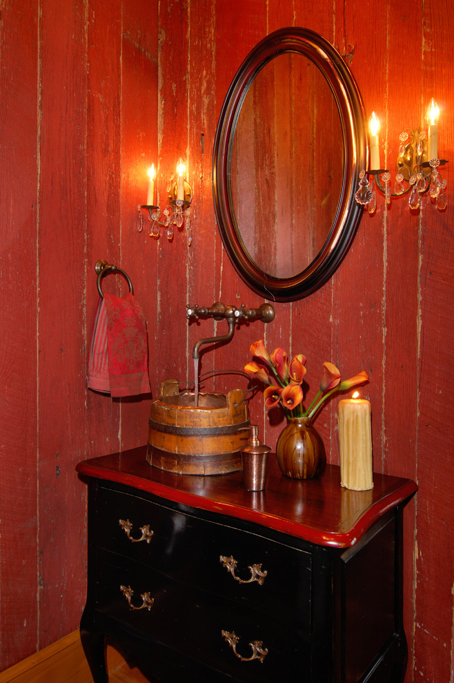 Rustik inredning av ett litet röd rött toalett, med ett fristående handfat, möbel-liknande, svarta skåp, träbänkskiva, röda väggar och mellanmörkt trägolv