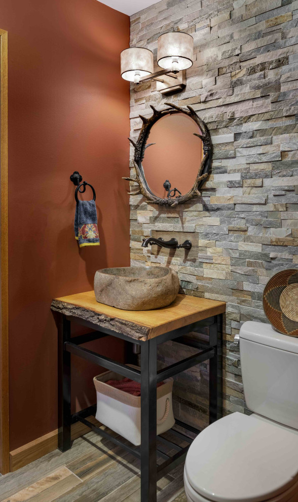 Inredning av ett rustikt litet toalett, med svarta skåp, träbänkskiva, öppna hyllor, en toalettstol med separat cisternkåpa, flerfärgad kakel, orange väggar, ett fristående handfat och flerfärgat golv